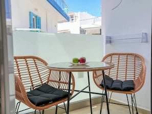 Ein Balkon mit zwei Korbstühlen, einem Glastisch und einem Teller mit Äpfeln.