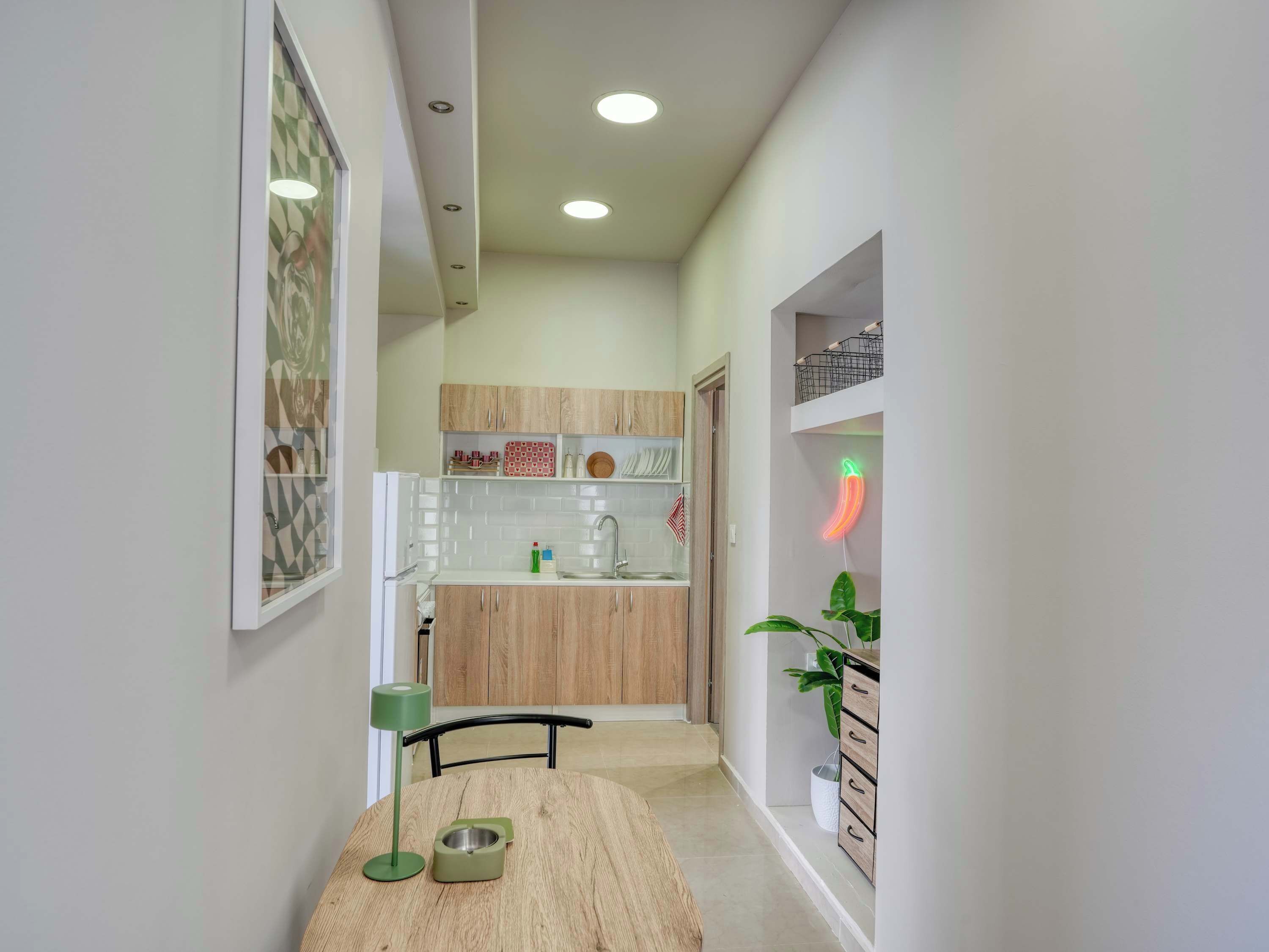 A narrow hallway leading to a kitchen with wooden cabinets, a sink, and a neon chili sign.