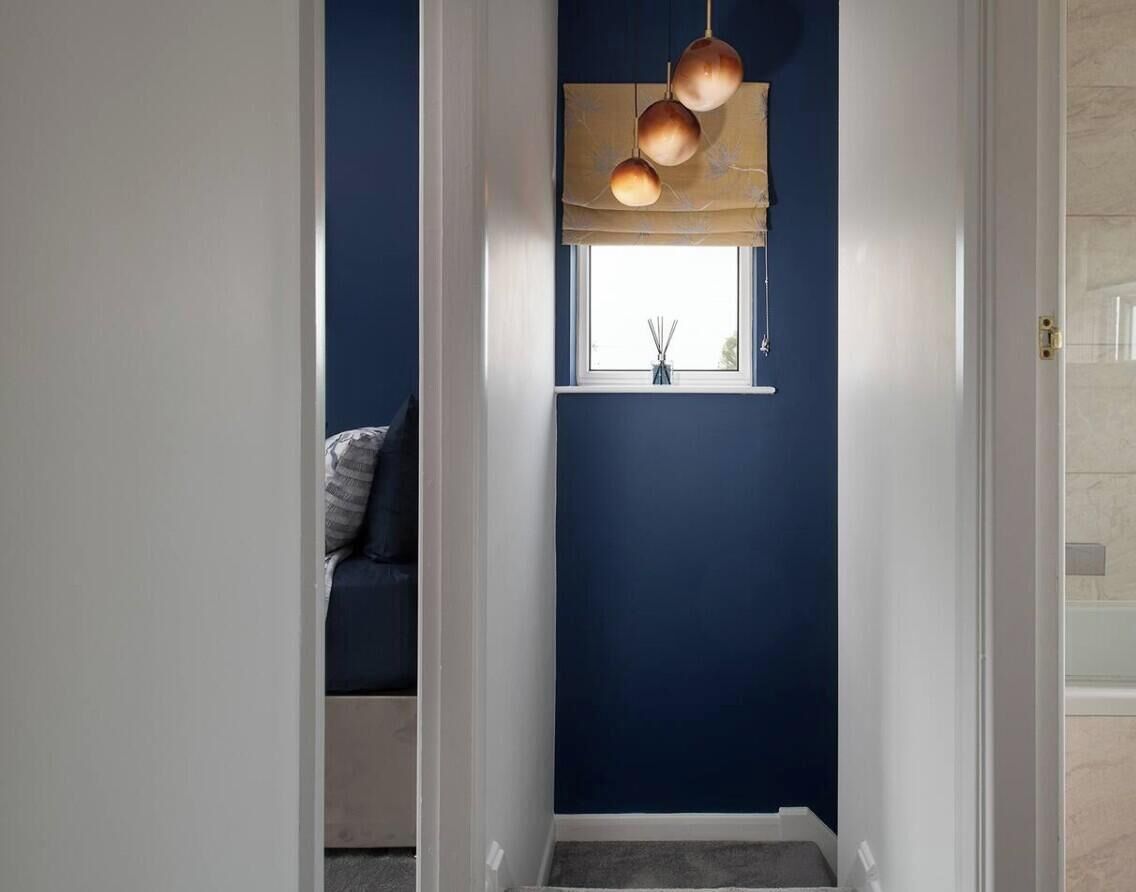 Un couloir avec un mur bleu foncé, une fenêtre donnant sur un paysage et un luminaire suspendu.