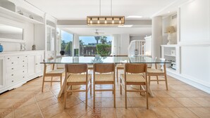 Una cocina amplia con mesa de vidrio, sillas de madera y muebles de cocina blancos.