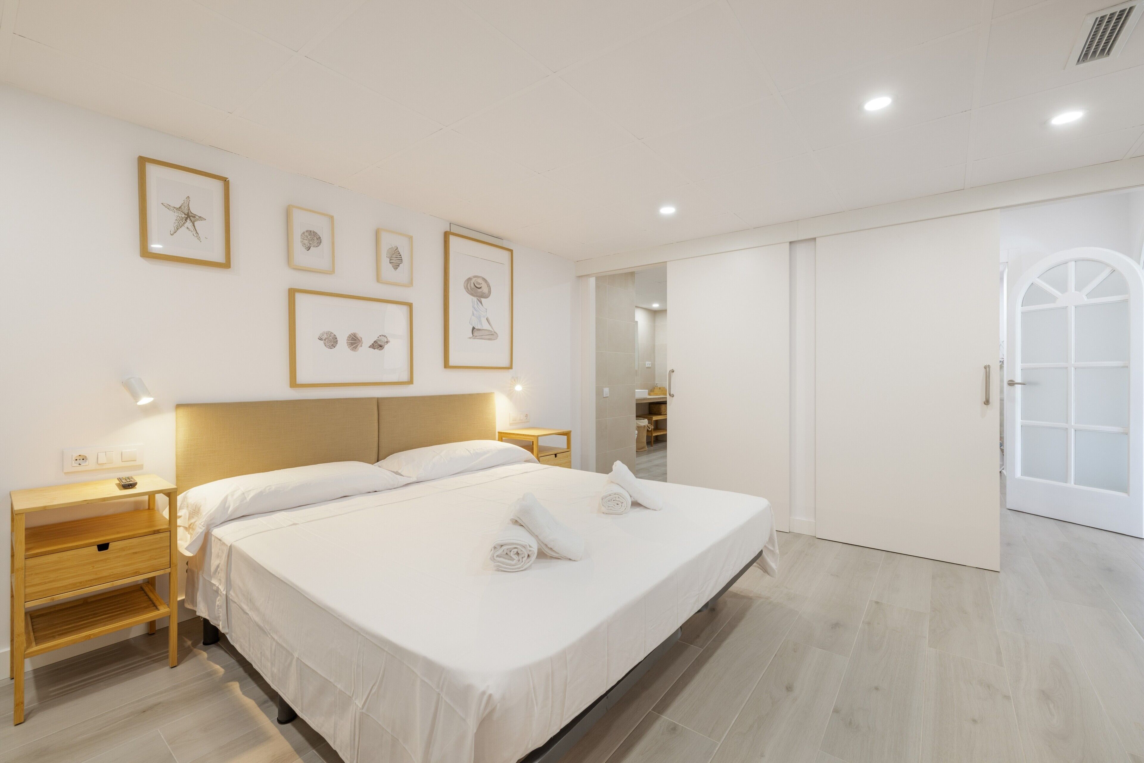 Ett hotellrum med en stor säng, sängbord, en garderob och inramade konstverk på väggen.