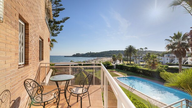 Un balcón con mesa y sillas, una piscina y vistas a la playa y al mar.