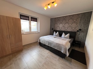 A bedroom with a bed, a wardrobe, a window, and a patterned wall.