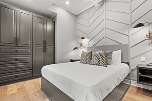 A modern bedroom with a large bed, built-in wardrobe, and a geometric wall design.