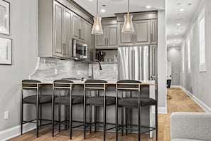 A modern kitchen with grey cabinets, stainless steel appliances, and bar stools.