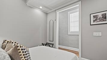 Un dormitorio con cama, una silla, una ventana con persianas, un cuadro en la pared y un interruptor de luz.