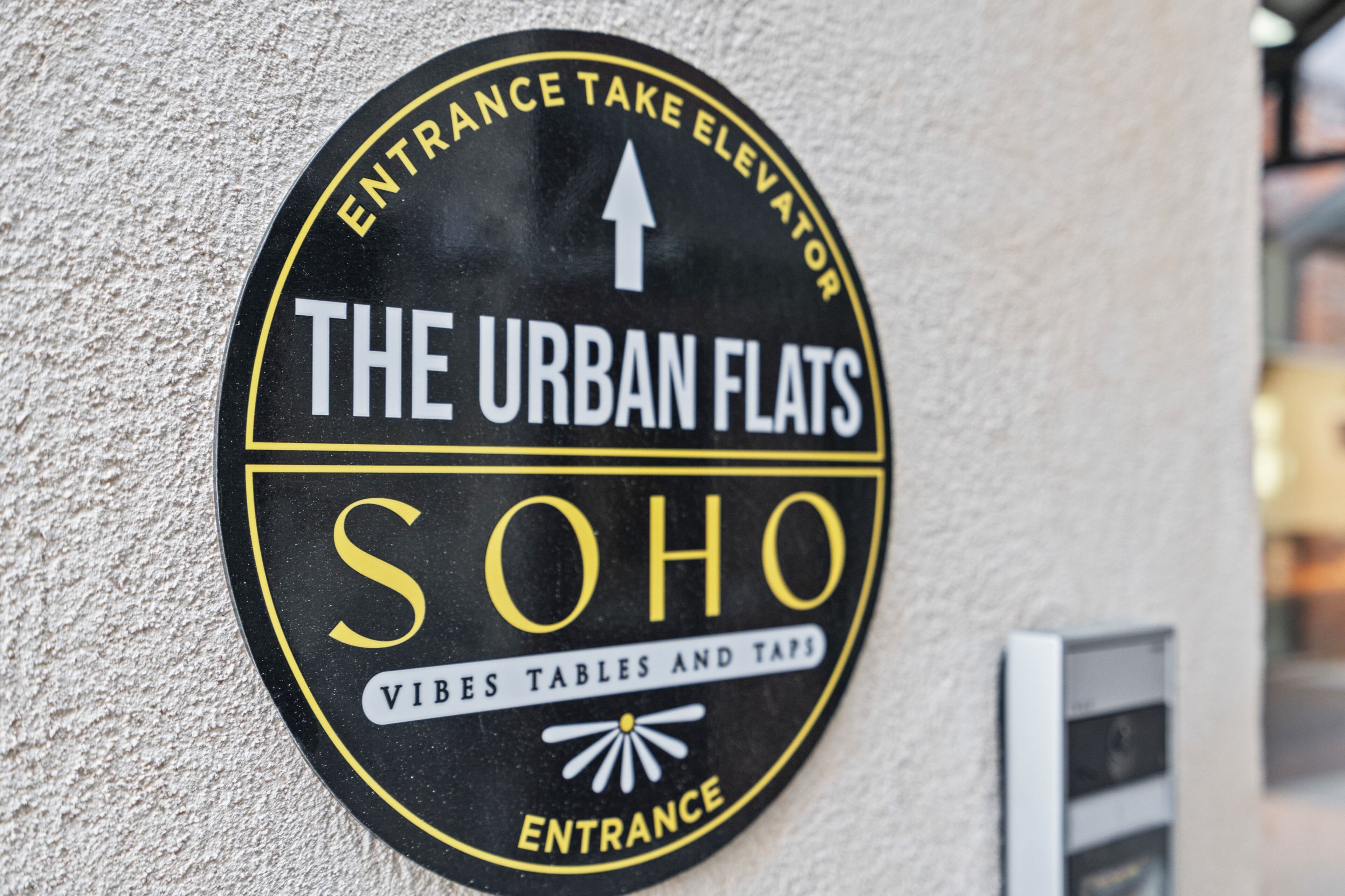 A circular sign with text indicating an entrance to The Urban Flats Soho, featuring vibes tables and taps.