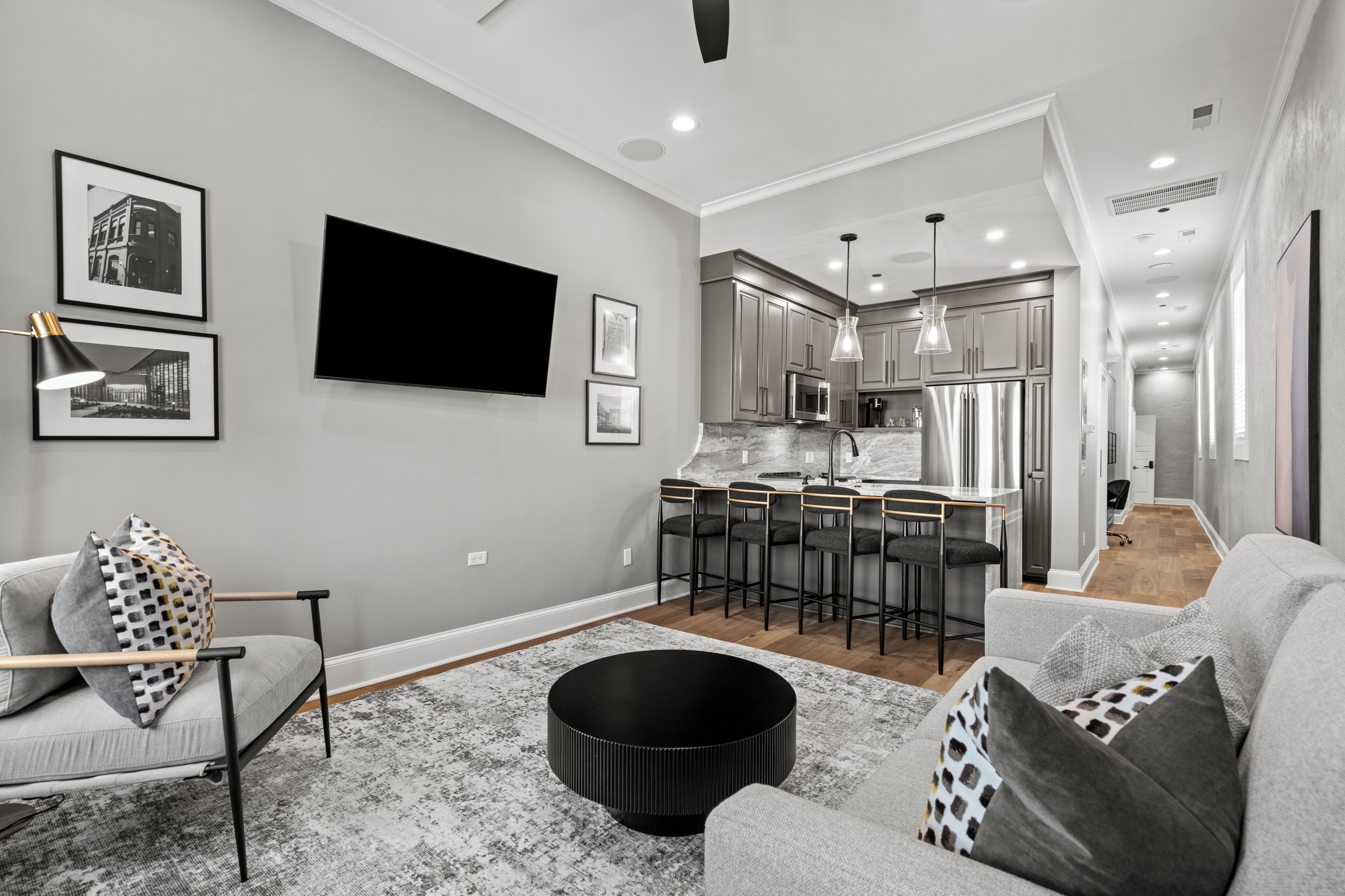 A modern living room with a grey sofa, a black ottoman, and a bar area with stools.