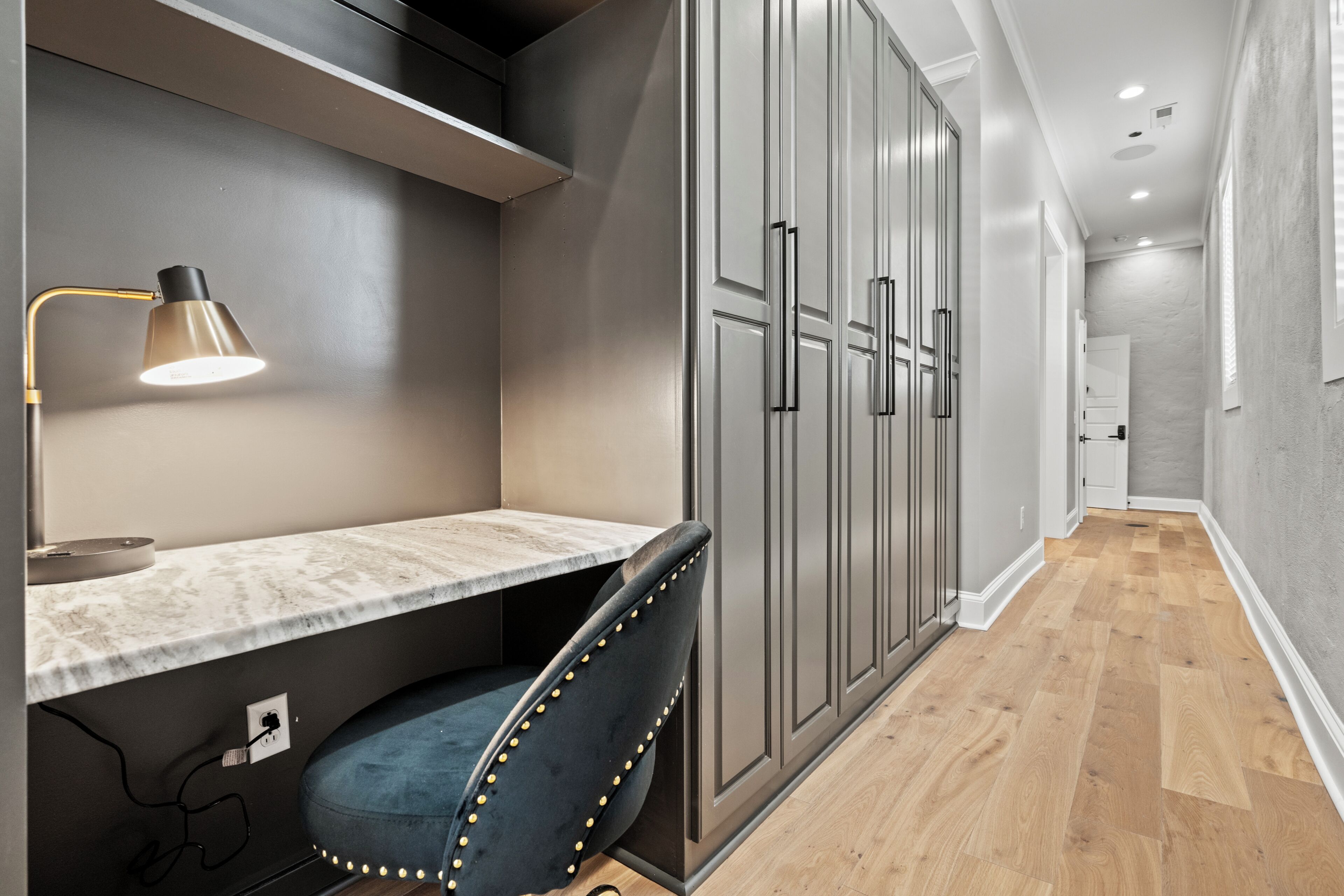 Una cocina moderna con encimera de mármol, una lámpara colgante, un sillón tapizado en azul y armarios grises.