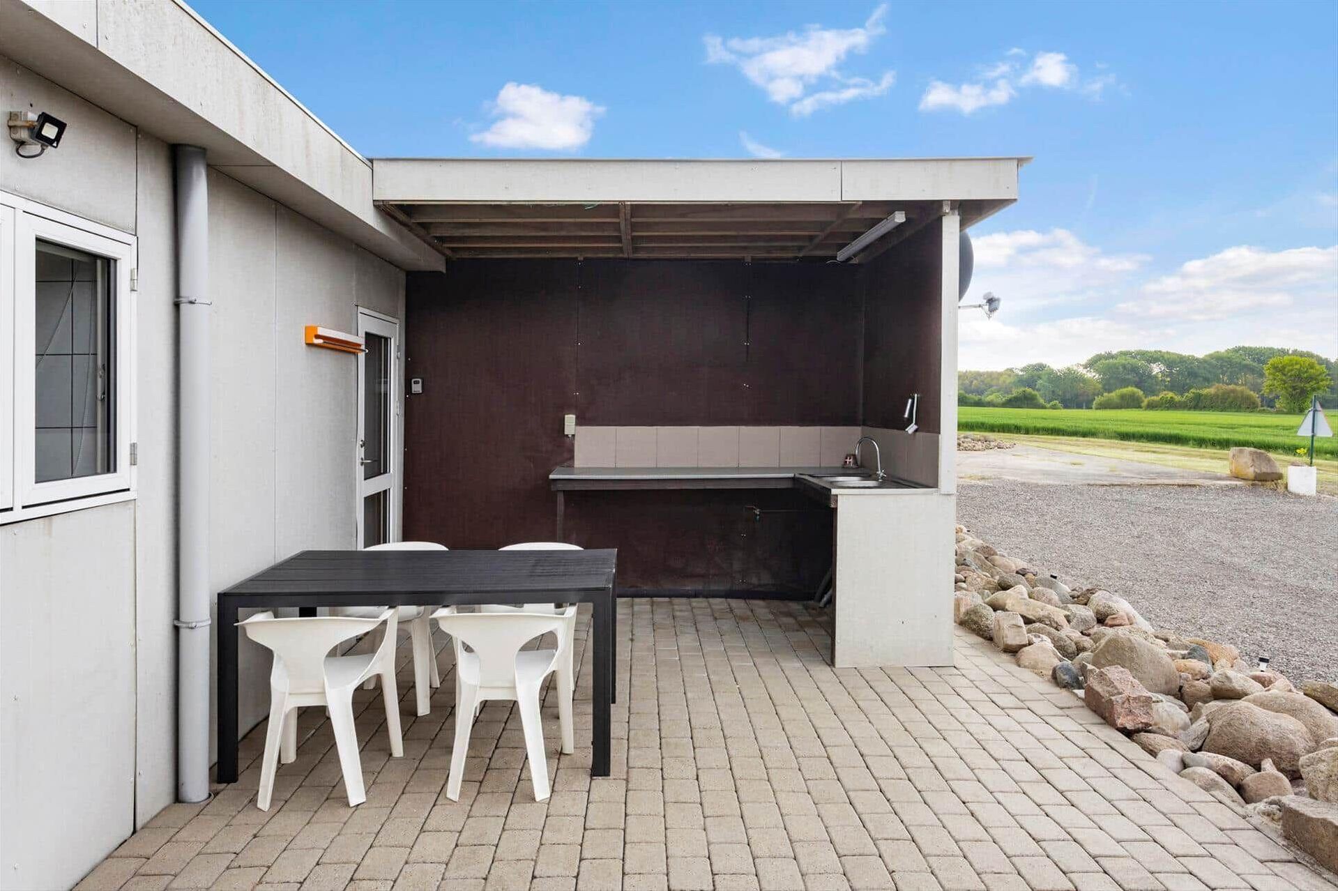 An outdoor kitchen area with a table and chairs, a sink, and a view of the countryside.
