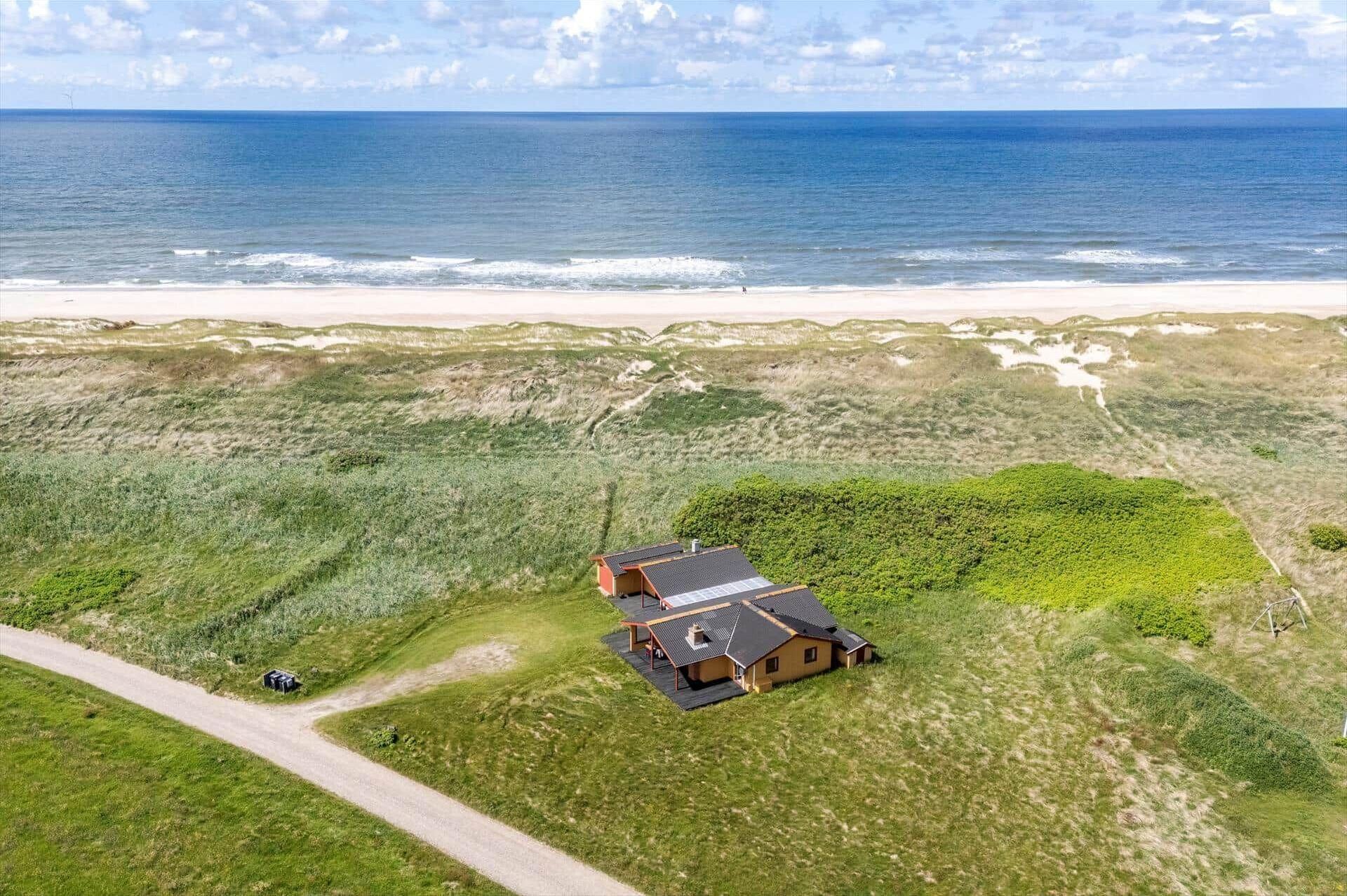 An aerial view of a house with a beach view, surrounded by grassy terrain.