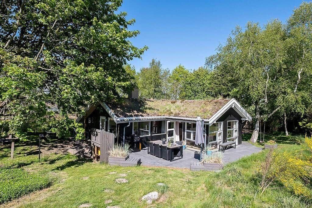 A house with a covered patio, a deck, and a large window overlooking a grassy area.