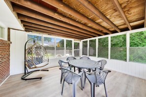 Un patio couvert avec une table ronde et des chaises, de grandes fenêtres et un fauteuil suspendu.