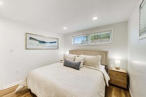 Une chambre à coucher avec un lit, une table de chevet, une fenêtre et un tableau accroché au mur.
