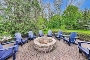 A circular fire pit with seating around it, surrounded by greenery and trees.