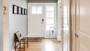 Un pasillo con una puerta blanca, cuadros enmarcados, una pequeña mesa con un cuadro y una silla.