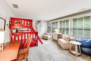 A room with a bunk bed, a sofa, a small table, and a window with blinds.
