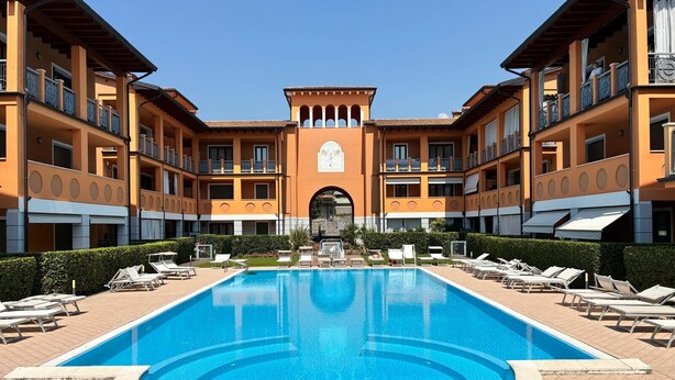 Une grande piscine avec des chaises longues et, au fond, un bâtiment doté de balcons.