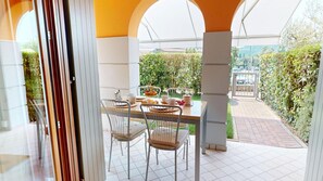An outdoor dining area with a table set for two, surrounded by metal chairs, under a covered patio with a view of a garden and a gate. - Freestyle Apartment By Bookinggardalake (Salò)