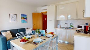 Une cuisine moderne avec des meubles blancs, une table à manger dressée pour deux personnes et un canapé dans l’espace salon.