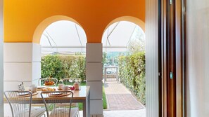 An outdoor dining area with a table set for two, a view of a garden, and a building in the background. - Freestyle Apartment By Bookinggardalake (Salò)