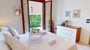 Ein Hotelzimmer mit Bett, Nachttisch mit Tablett für Toilettenartikeln, Schreibtisch mit Stuhl und Blick auf einen Garten durch eine geöffnete Tür.