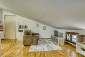 A loft-style room with a wooden floor, a brown sofa, a small kitchenette, a television, and a window with a view. - The Refuge of Manu - Lucca (Lucca)