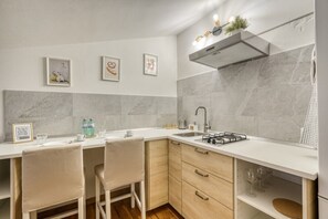 A modern kitchen with a white countertop, two bar stools, a gas stove, a sink, and a stainless steel range hood. - The Refuge of Manu - Lucca (Lucca)
