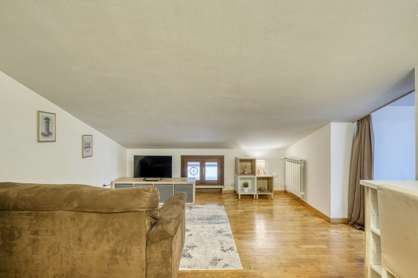 Un salon spacieux comprenant un canapé, un téléviseur, un radiateur et une fenêtre avec des rideaux.