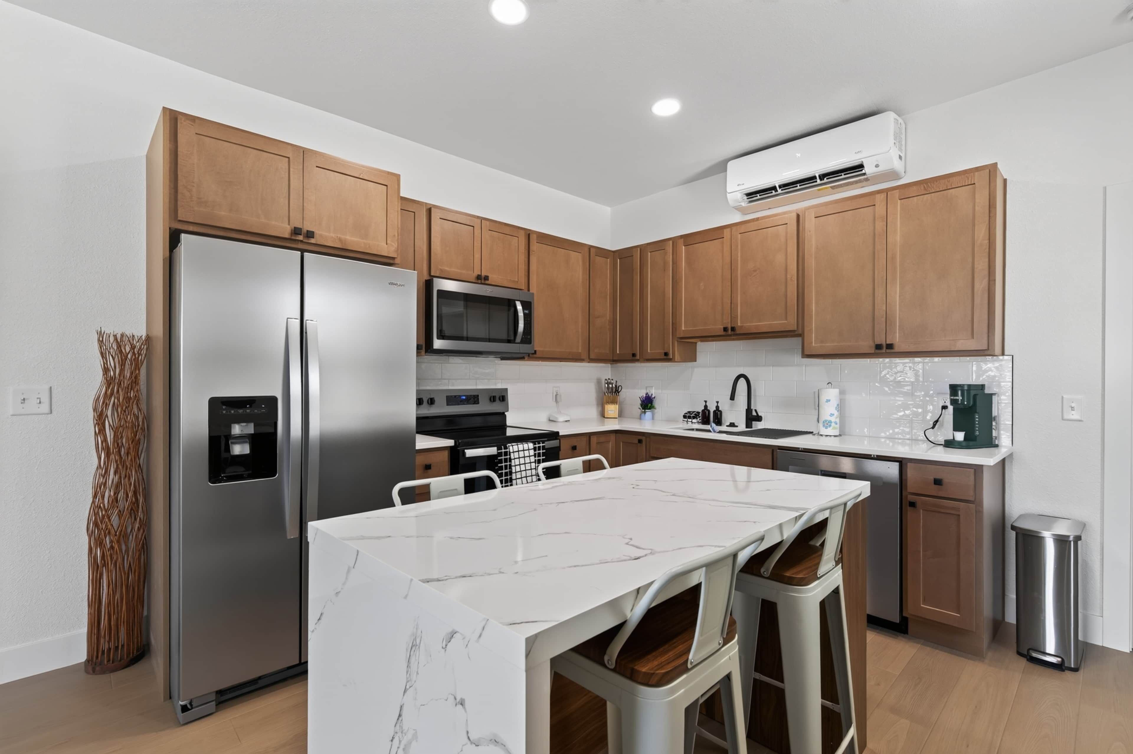 A modern kitchen with stainless steel appliances, wooden cabinets, and a marble island.