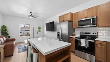 A modern kitchen with a central island, stainless steel appliances, wooden cabinets, and a view of a residential area.