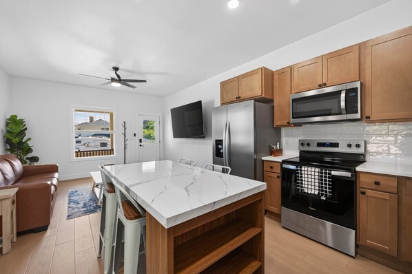A modern kitchen with a central island, stainless steel appliances, wooden cabinets, and a view of a residential area.