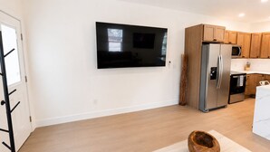 A modern kitchen with a built-in TV, stainless steel appliances, wooden cabinets, and a light-colored floor.