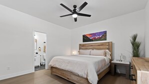A bedroom with a wooden bed, a ceiling fan, a nightstand, a lamp, and a painting on the wall.