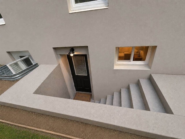 A modern building with a central staircase, a door with a 'WELCOME' mat, and small windows.