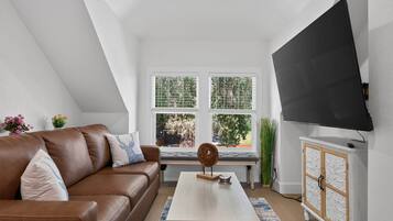 A modern living room with a brown leather sofa, a white coffee table, and a large flat-screen TV mounted on the wall.