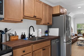 A modern kitchen with wooden cabinets, a stainless steel refrigerator, a sink, and a countertop with various kitchen items.