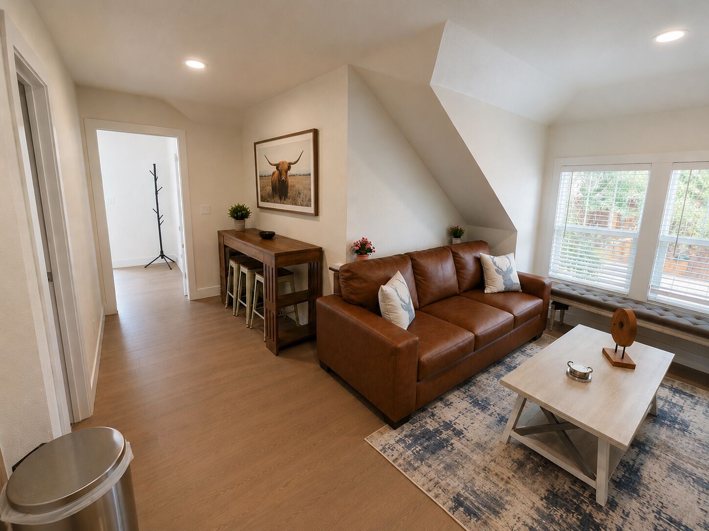 Un salon avec un canapé en cuir marron, une table basse, un coin repas avec une table et des tabourets en bois, et un tableau représentant un taureau accroché au mur.