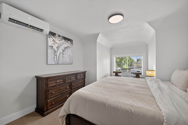 A bedroom with a bed, dresser, and an air conditioning unit on the wall.