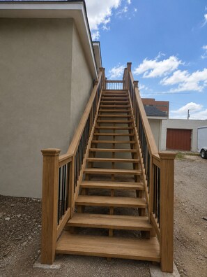 Una escala de fusta amb barana que mena a un edifici amb façana de color beix.
