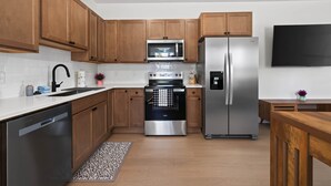 A modern kitchen with wooden cabinets, stainless steel appliances, and a black refrigerator.