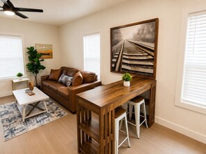 A modern living room with a brown leather sofa, a wooden coffee table, and a dining area with a wooden table and bar stools.