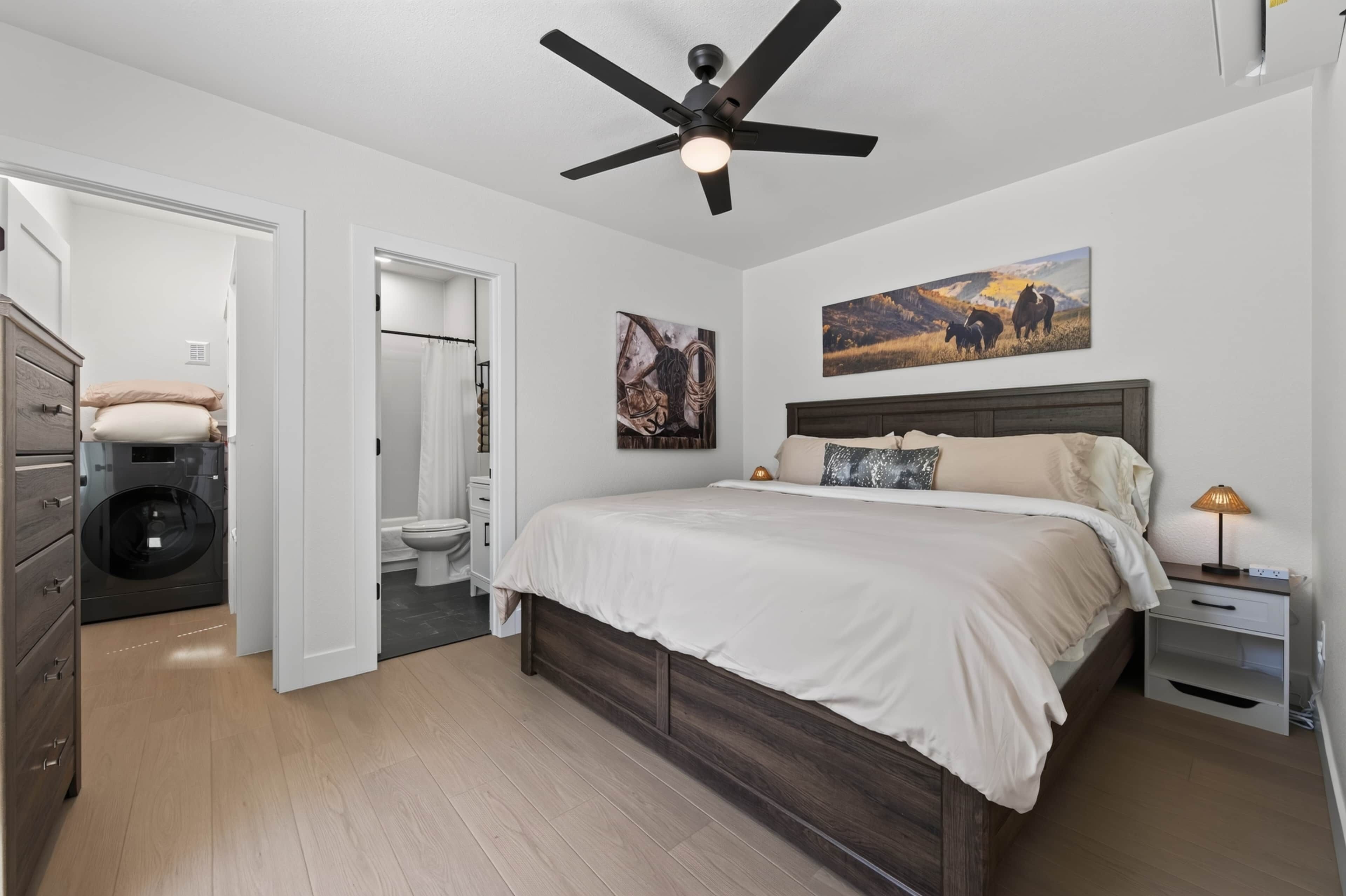 A bedroom with a bed, a ceiling fan, a nightstand, and a painting on the wall.