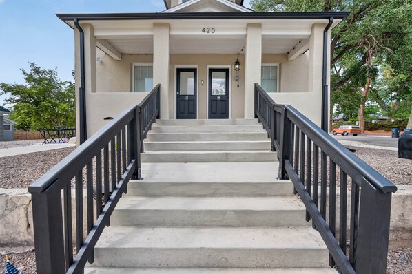 A building with a double door entrance, a set of concrete steps, and a black metal railing.