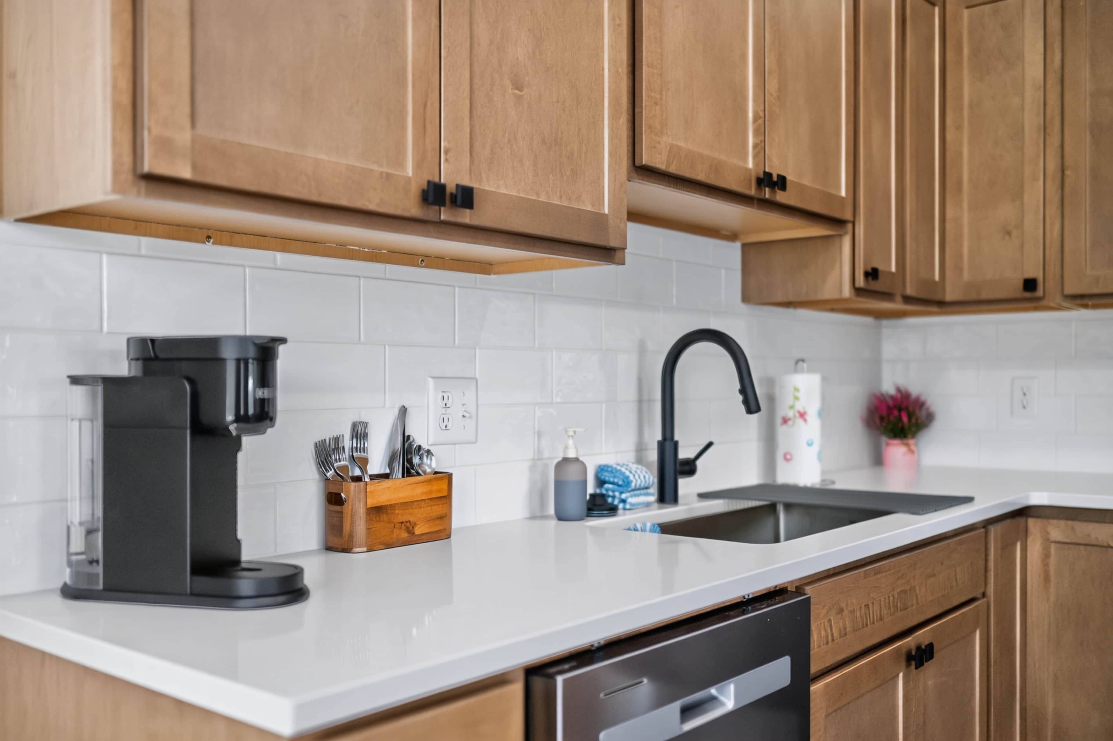 Una cucina moderna con mobili in legno, un piano di lavoro bianco, una macchina per il caffè, un lavello e un espositore per piatti.