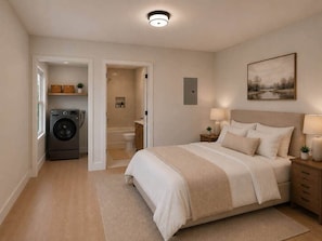 A bedroom with a bed, bedside tables, a nightstand, a lamp, a painting on the wall, a washing machine, and a bathroom visible through an open door. - Spurs & Serenity on 23rd st (Cheyenne)