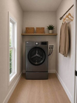 A compact laundry room with a front-loading washing machine, a shelf with baskets and a potted plant, and a drying rack with clothes. - Spurs & Serenity on 23rd st (Cheyenne)