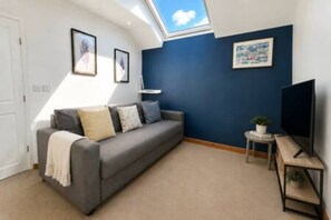 Ein Zimmer mit einer grauen Couch, einem kleinen Tisch mit einer Pflanze, einem Fernseher und gerahmten Bildern an der Wand.