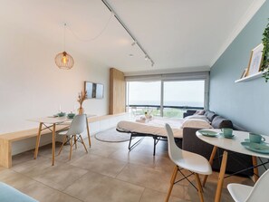 Ein modernes, helles Zimmer mit großem Fenster, Essbereich und Bett mit Blick.