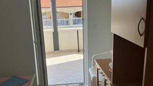 Ein Zimmer mit einer Schiebeglastür, die zu einem Außenbereich mit gefliestem Boden führt, mit einem Gebäude mit rotem Dach im Hintergrund.